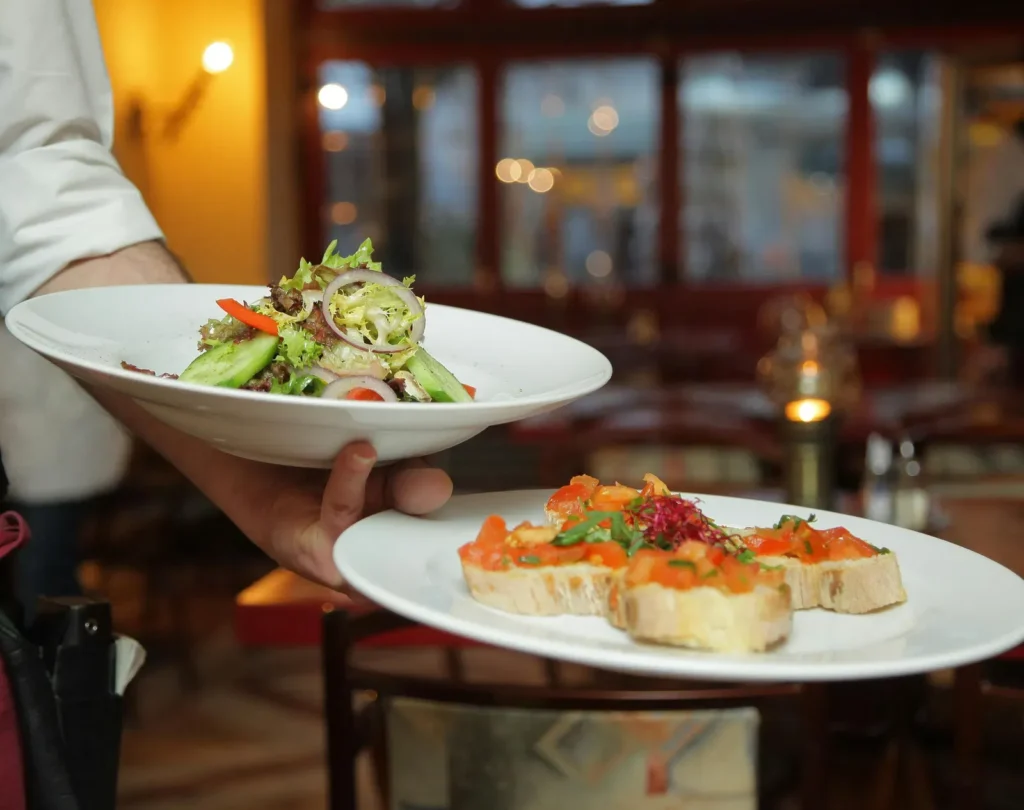 a person in a restaurant holding two plates with delicious dishes in it that are well plated a2933490